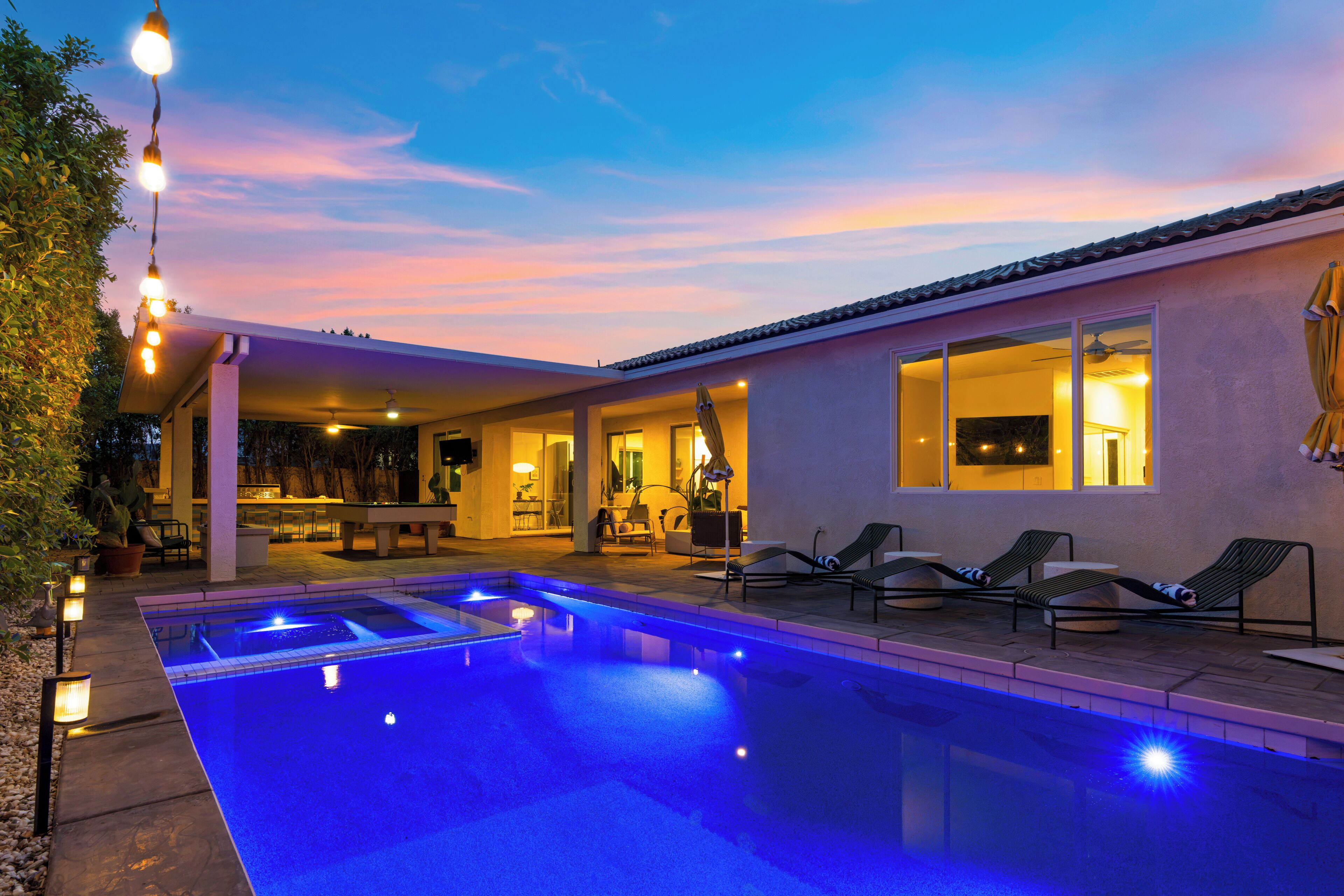 A swimming pool with a patio area, lounge chairs, and a covered seating area with a view of the pool.