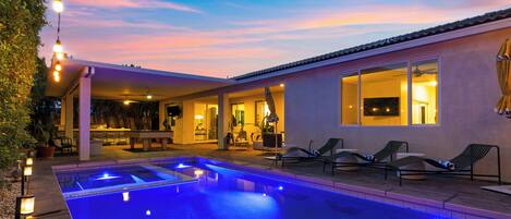 A swimming pool with a patio area, lounge chairs, and a covered seating area with a view of the pool.