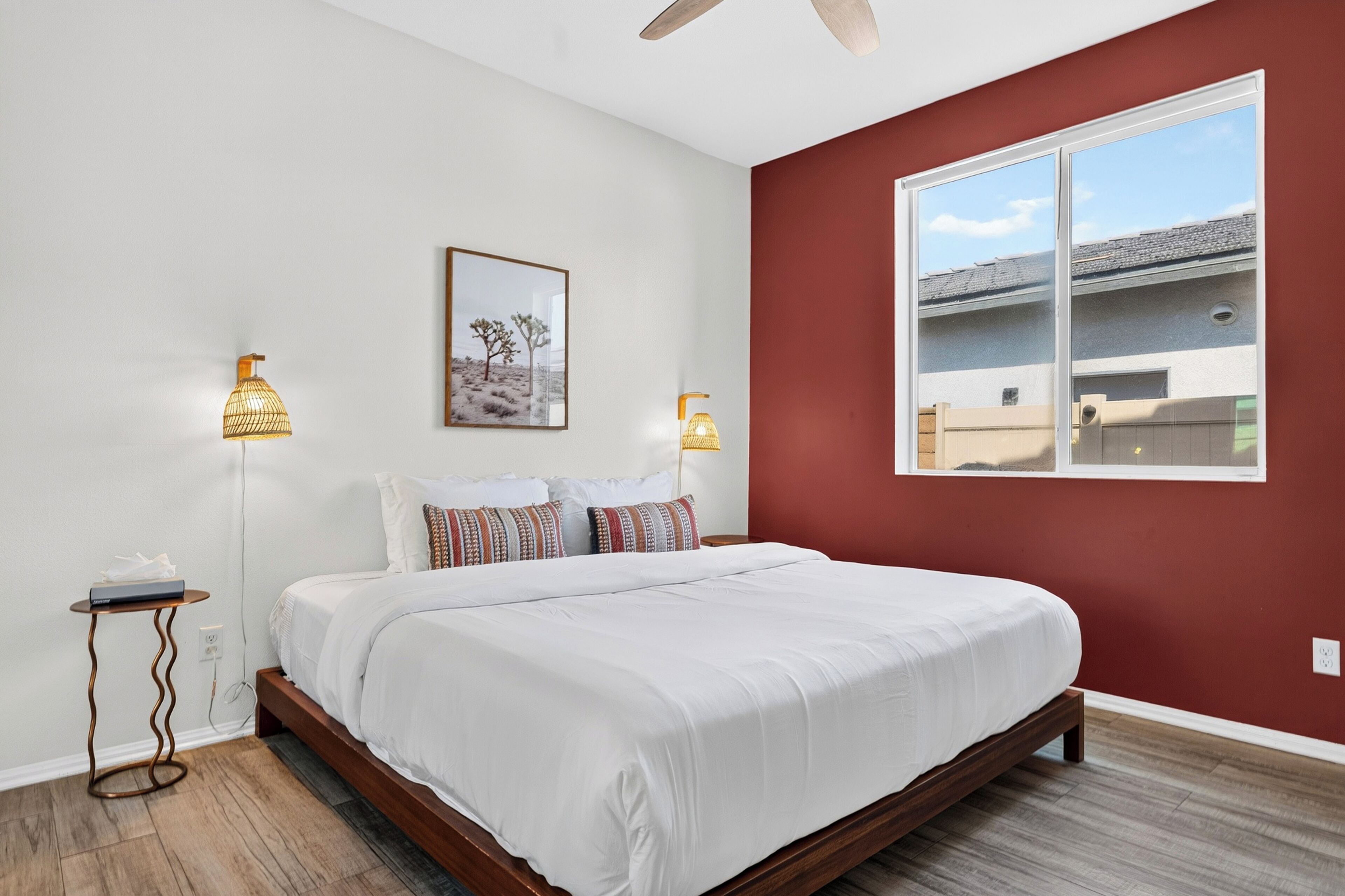 A bedroom with a bed, two bedside lamps, a framed picture on the wall, and a window with a view of a building.