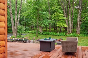 Terraza de madera con mobiliario exterior, que incluye una mesa y sillas, con vistas a una zona boscosa.