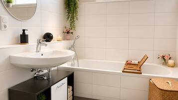 Une salle de bain moderne avec un lavabo blanc, une baignoire, un miroir et une plante en pot.