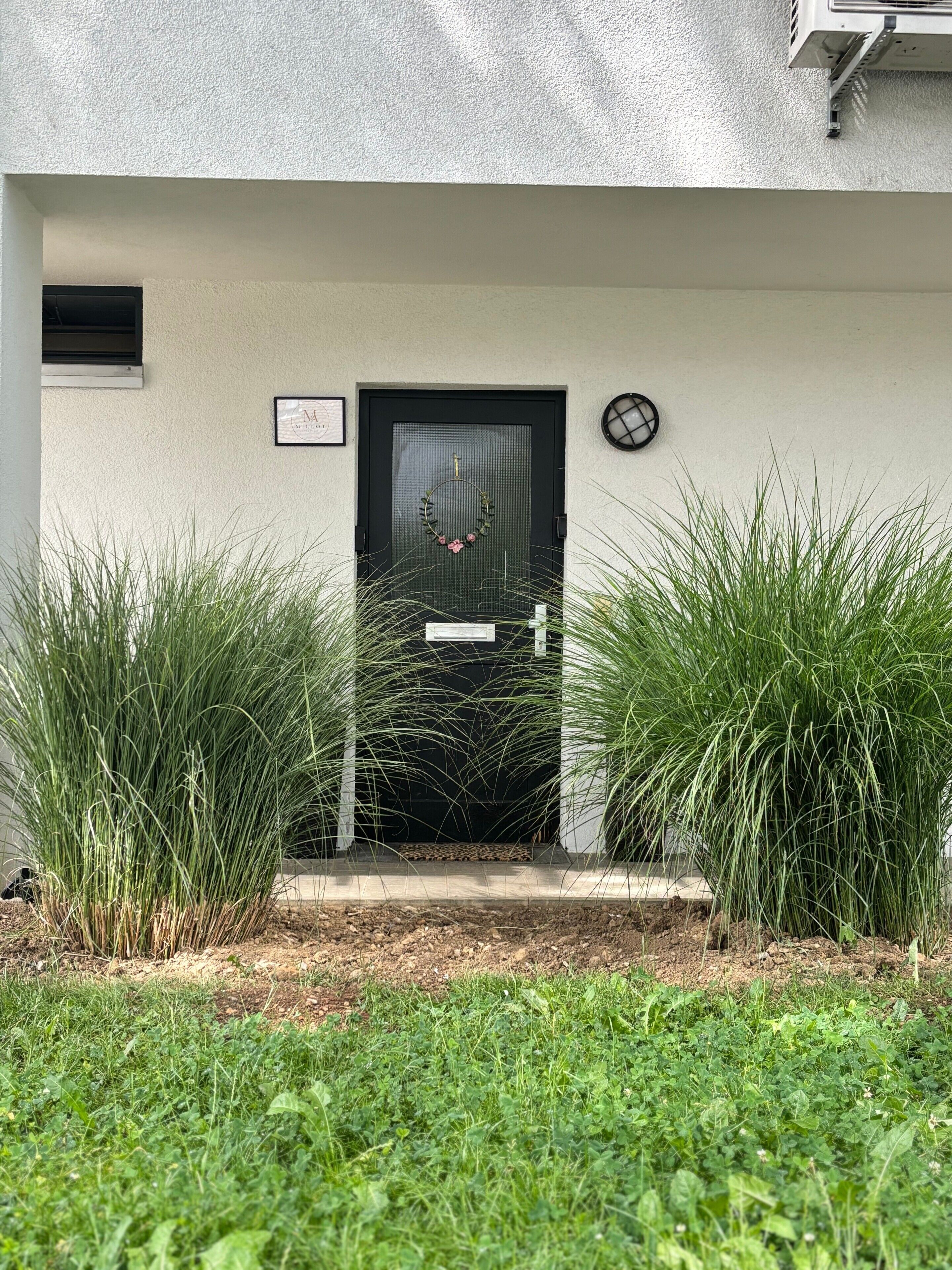 A modern building entrance with a black door, a welcome sign, and a small window.