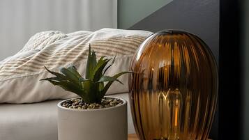 A room with a bed, a potted plant, a decorative lamp, and a salt lamp on a wooden side table.