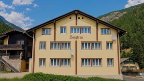 Un hotel de diverses plantes amb una entrada central, balcons i un paisatge de muntanyes al fons.