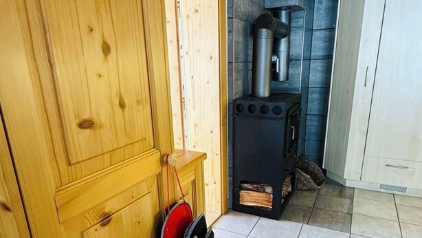Interior de fusta amb terra de rajola, una estufa negra i una bossa vermella penjada a la paret.