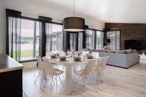 A modern living room with a dining area, large windows, and a flat-screen TV. - Christmas 4BR Villa Private Sauna By Lapland Host (Rovaniemi)