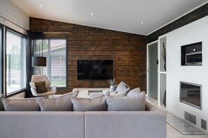 A modern living room with a sectional sofa, a television, and a fireplace. - Christmas 4BR Villa Private Sauna By Lapland Host (Rovaniemi)