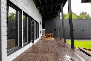 A covered outdoor area with a wooden deck, a table with chairs, and a view of a green lawn. - Christmas 4BR Villa Private Sauna By Lapland Host (Rovaniemi)
