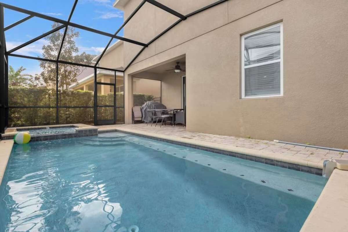 An outdoor swimming pool with a covered patio area, a table, and chairs.