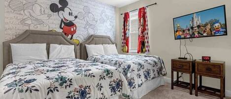 A bedroom with a Mickey Mouse themed wall, a bed with floral bedding, a nightstand, and a clock.