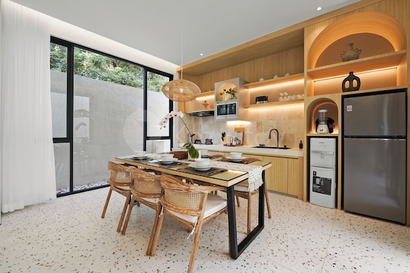 A modern kitchen with a dining area, featuring a large refrigerator, wooden cabinets, and a dining table with chairs.