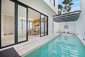 A modern outdoor pool area with a glass-enclosed dining space and a view of the interior.