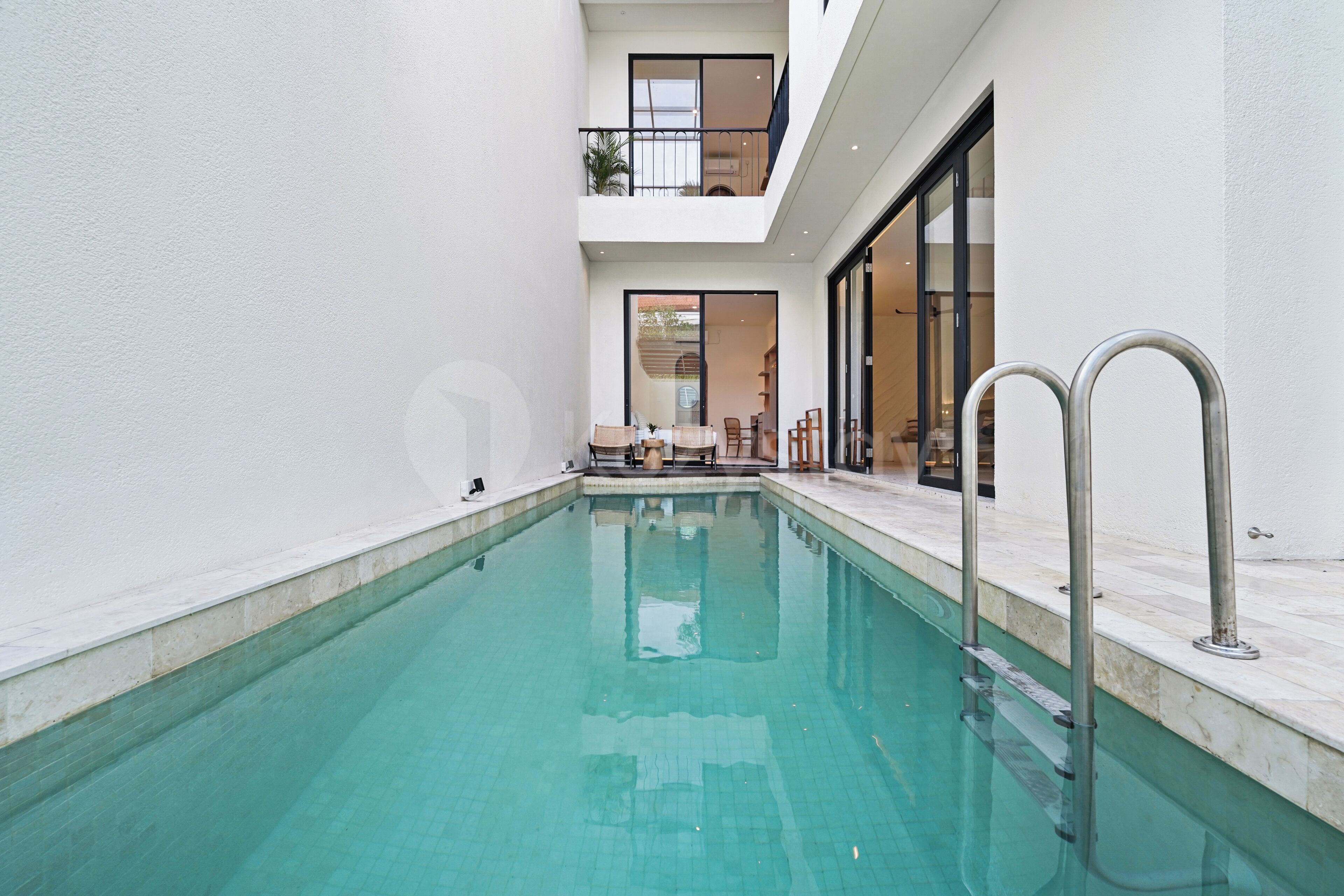 Piscina con agua azul cristalina, rodeada de paredes blancas y un balcón.