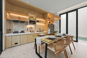 A modern kitchen with wooden cabinetry, a built-in microwave, and a dining area with a glass table and wicker chairs.