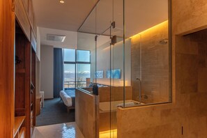 Una habitación de hotel moderna con cabina de ducha de vidrio, una cama, vistas a montañas y un armario de madera.