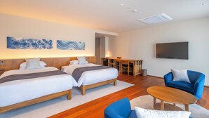 Habitación de hotel con dos camas, un escritorio, un televisor y un sillón azul.