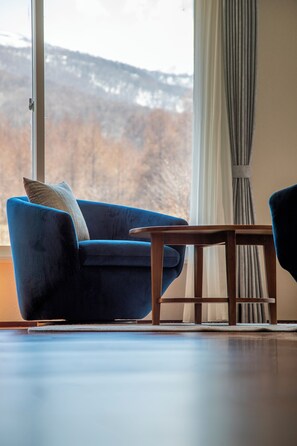 A room with a blue armchair, a wooden side table, and a view of a snowy landscape through a large window.