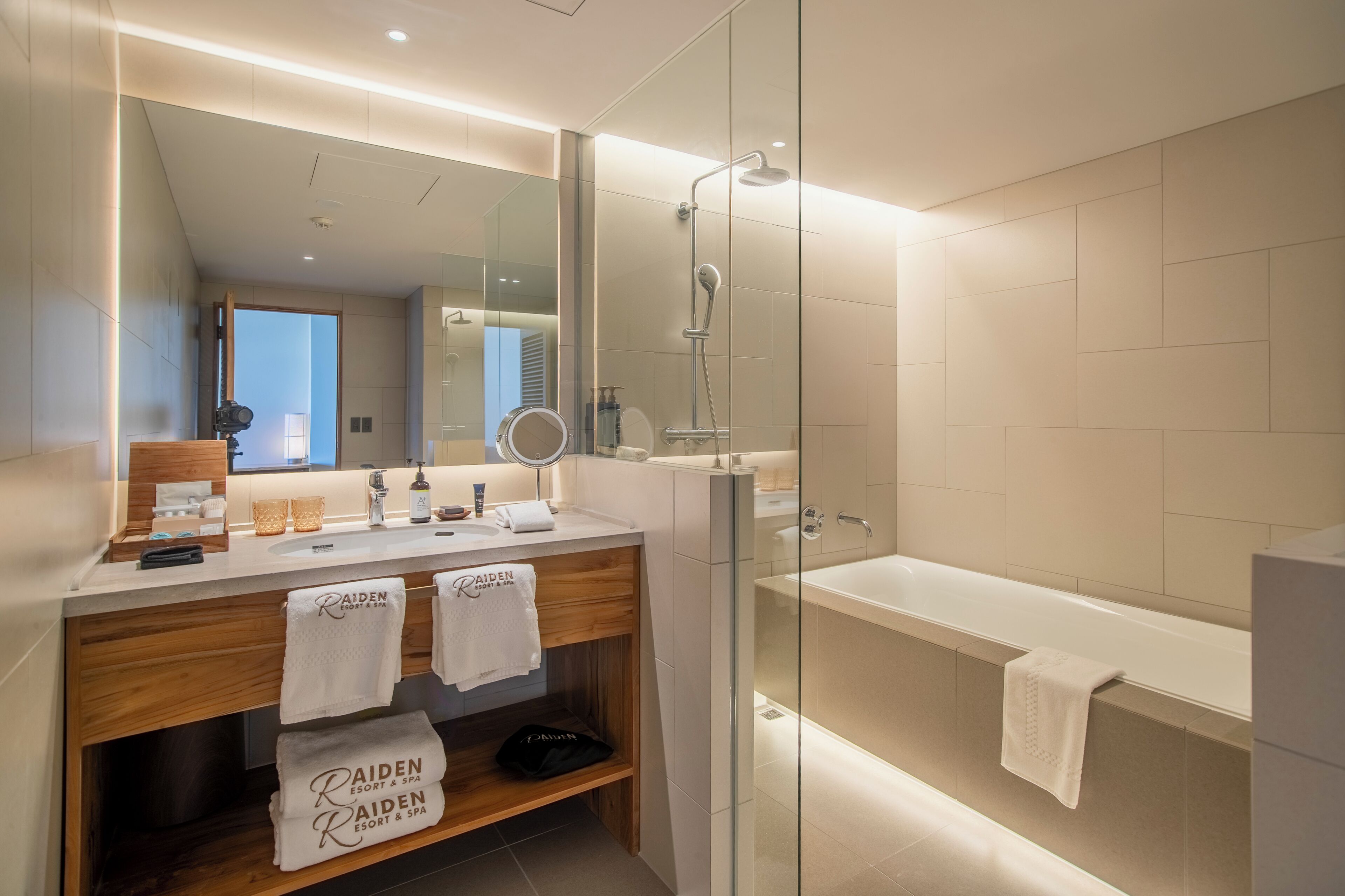 A modern bathroom with a glass-enclosed shower, a bathtub, and a vanity with a mirror and two sinks.