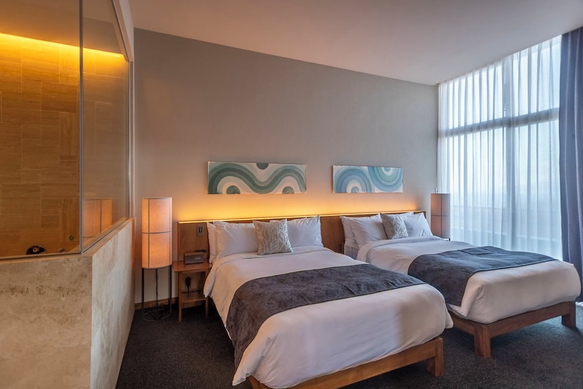 A hotel room with two beds, a large window, and artwork on the wall.