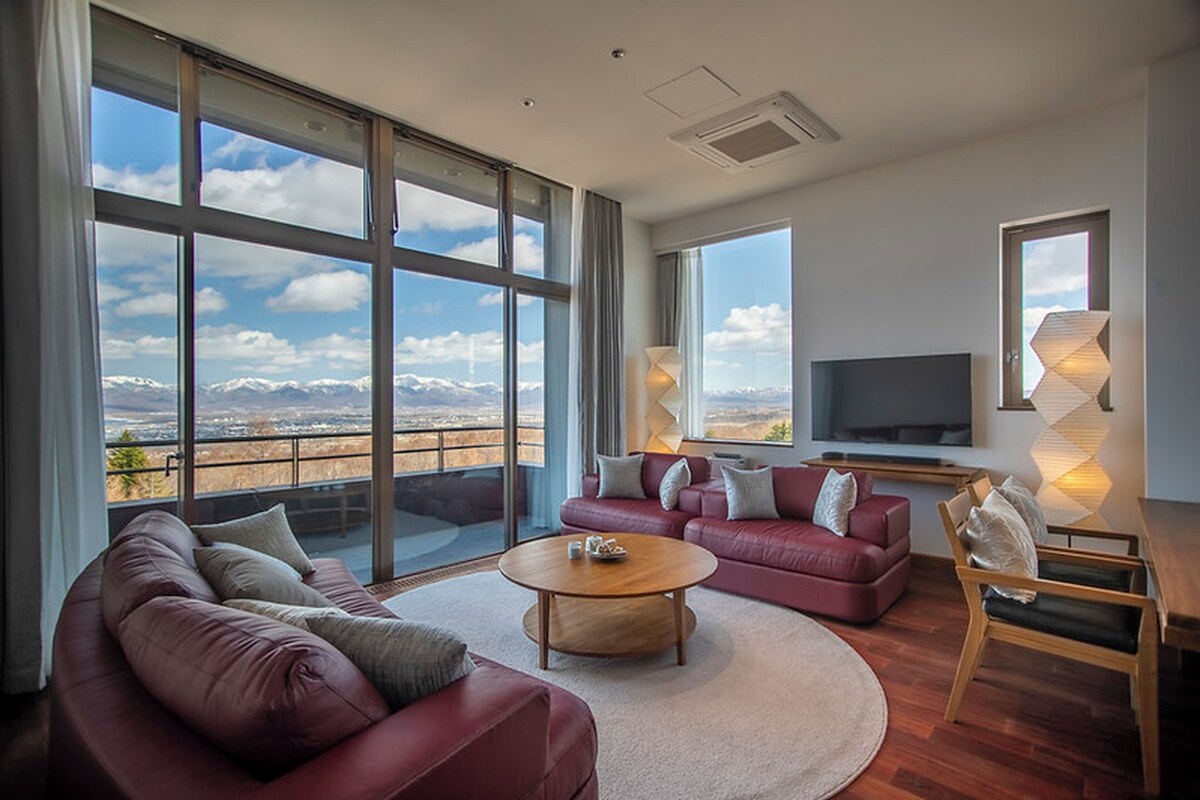 A modern living room with a large window, a flat-screen TV, and a red leather sofa.