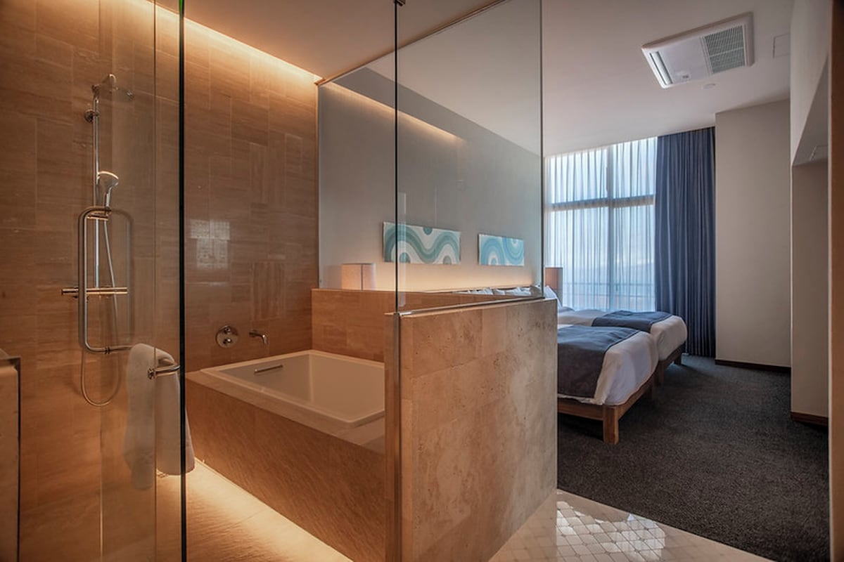 A modern hotel bathroom with a glass shower enclosure, a bathtub, and a large mirror.