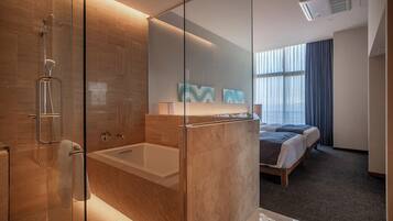 A modern hotel bathroom with a glass shower enclosure, a bathtub, and a large mirror.