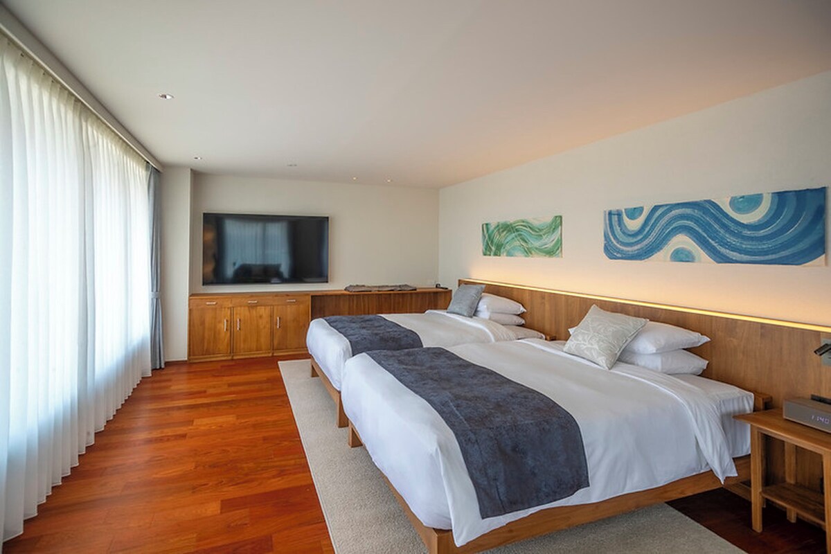 A modern bedroom with two beds, a television, and abstract wall art.