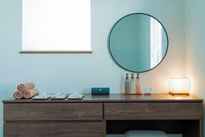 A hotel room with a wooden vanity, a round mirror, a window with blinds, and a bedside table with toiletries. - *NEW OPEN* 4-minute walk to Ikebukuro Station | Japandi, 125 ㎡, 3 bedrooms | 9 guests | 5 minutes to Shinjuku (Nishiikebukuro Toshima-ku)