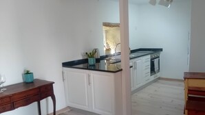 Quarto com cozinha equipada, armários brancos, mesa de madeira e um vaso com planta.