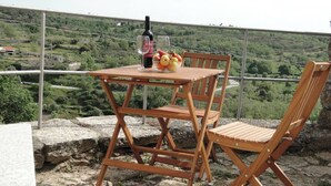 Conjunto de mesa e cadeira de madeira numa varanda com vista para uma paisagem verde.