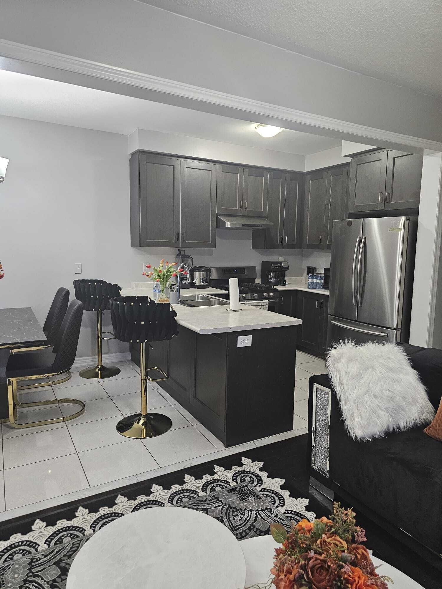 A modern kitchen with dark cabinets, a stainless steel refrigerator, and a dining area with black chairs and a white table.