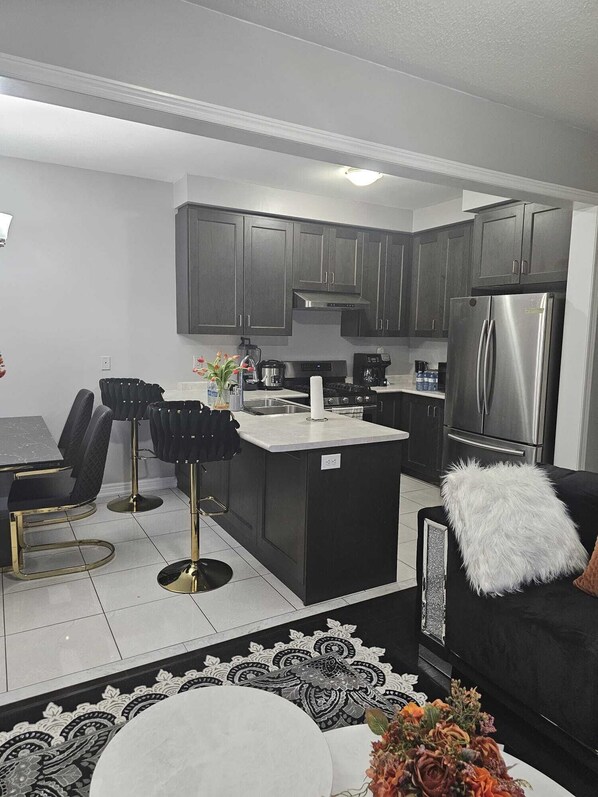 A modern kitchen with dark cabinets, a stainless steel refrigerator, and a dining area with black chairs and a white table.