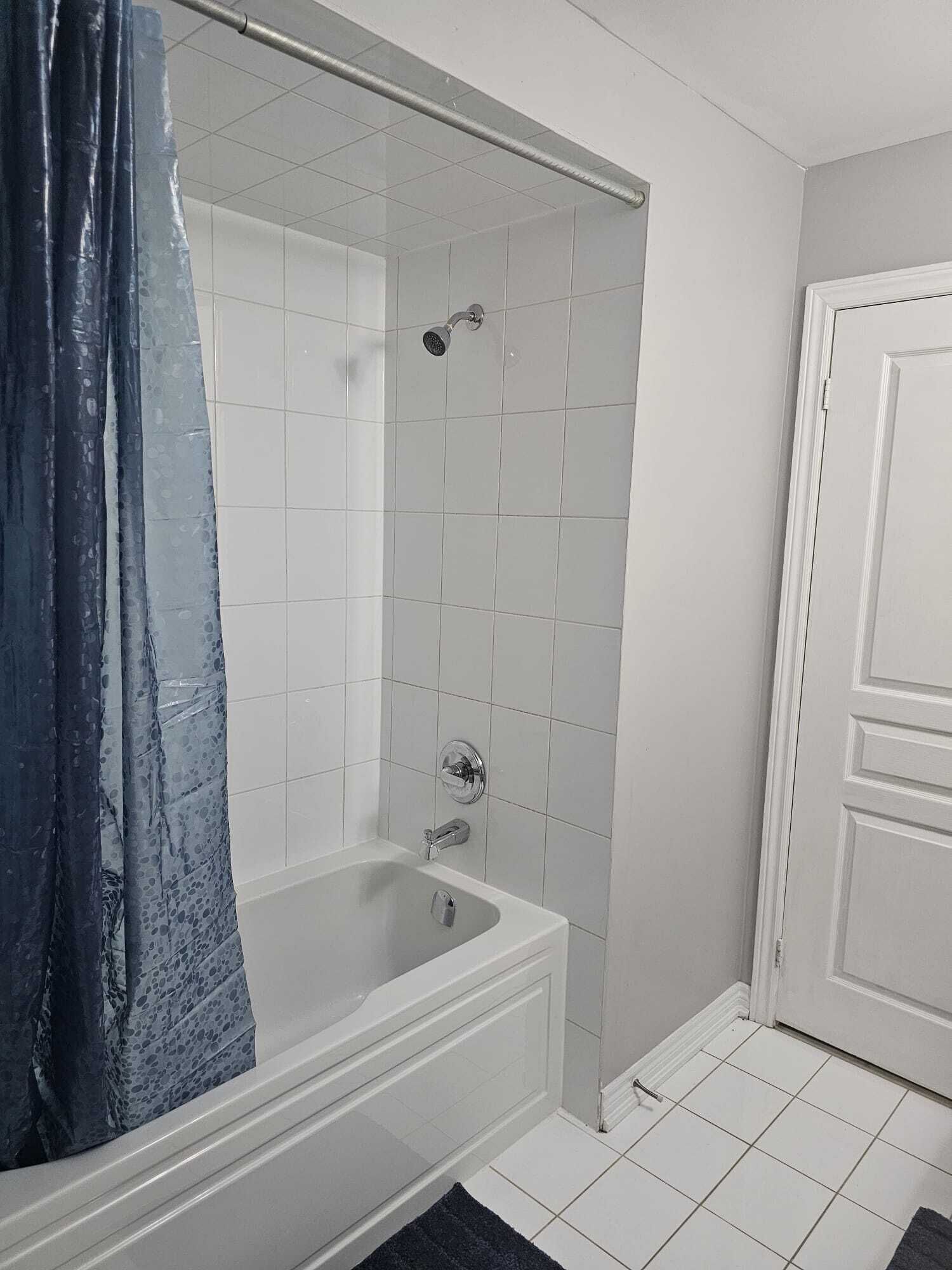 A bathroom with a bathtub, shower, and white tiled walls.