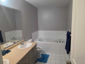 Un baño con bañera, dos lavamanos, inodoro y una alfombra de baño azul.