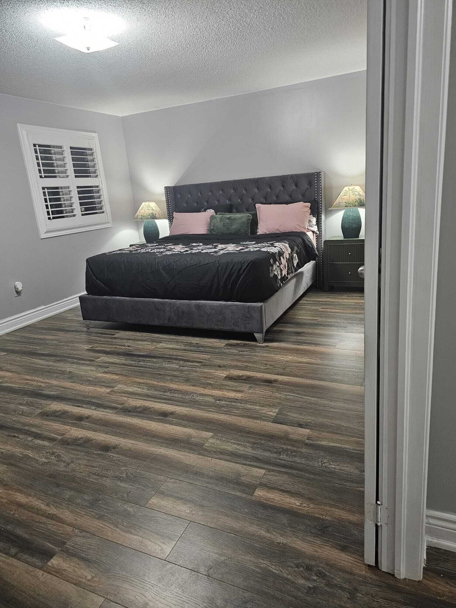 A bedroom with a large bed, two bedside tables, a window with blinds, and a ceiling light.