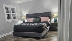 Een slaapkamer met een groot bed, twee nachtkastjes, een raam met zonwering en een plafondlamp.