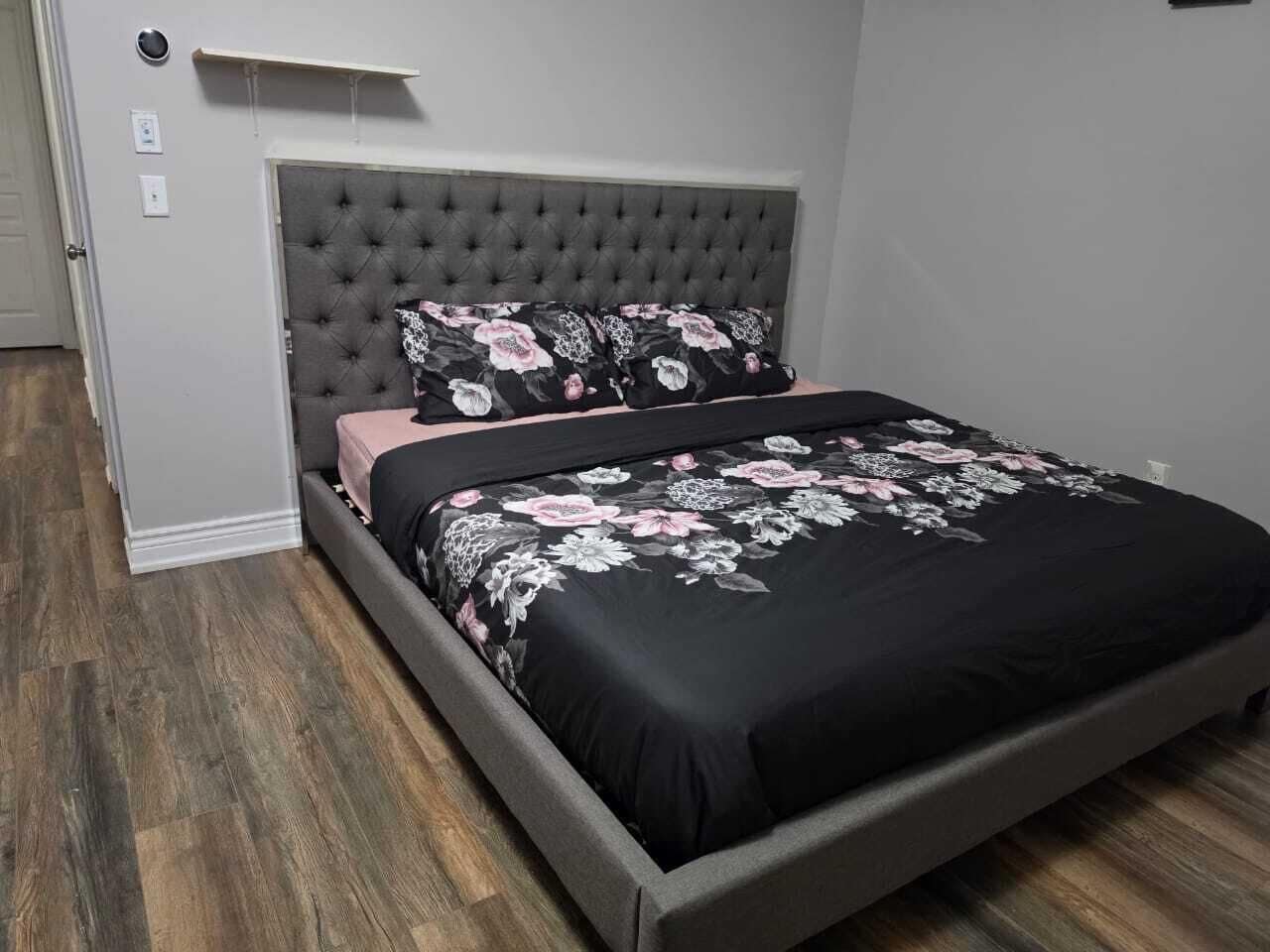 Un dormitorio con cabecera capitonada, cama con colcha floral y piso de madera.