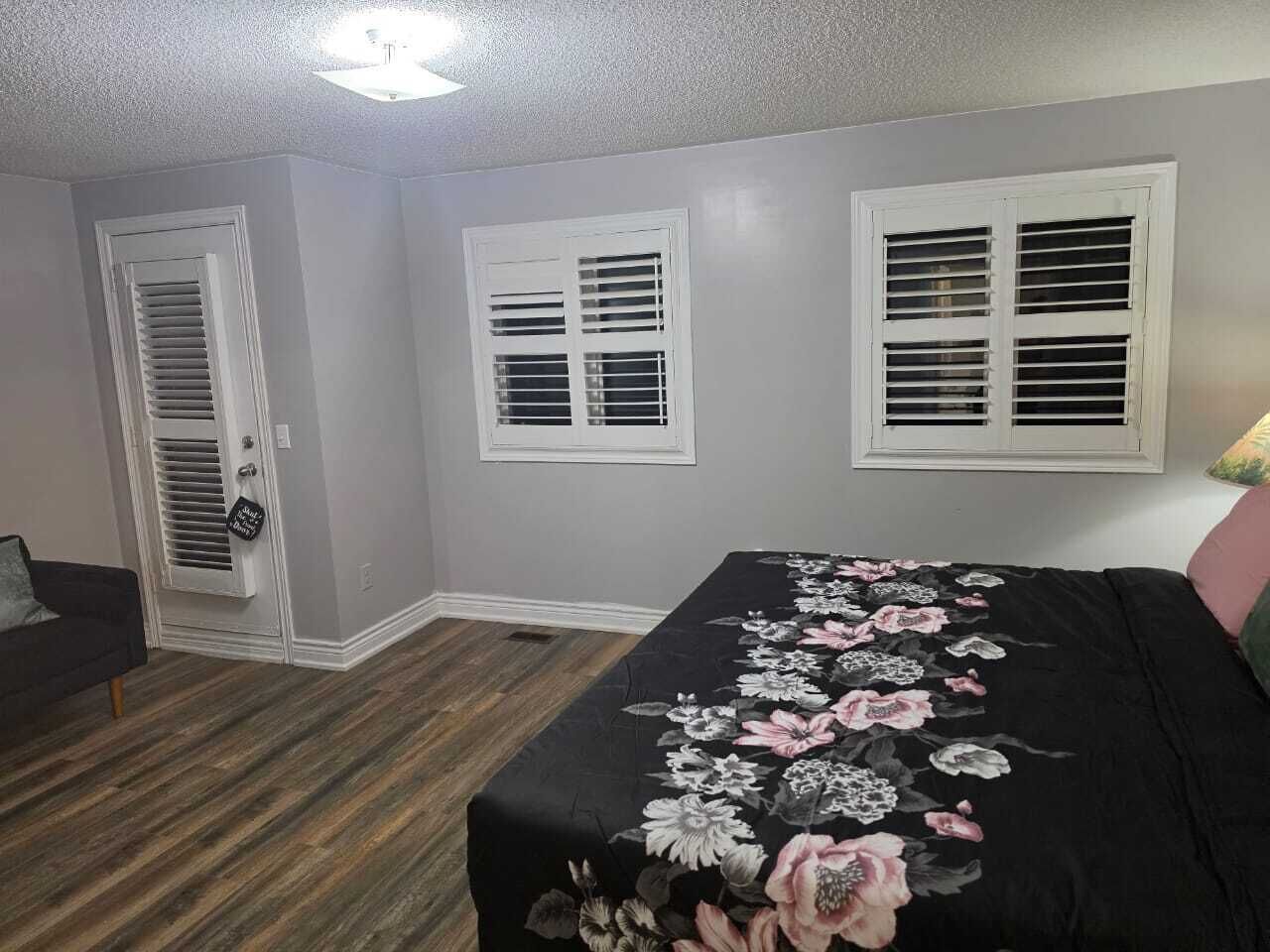 Une chambre à coucher avec un lit, deux fenêtres avec volets, une porte et un petit canapé.