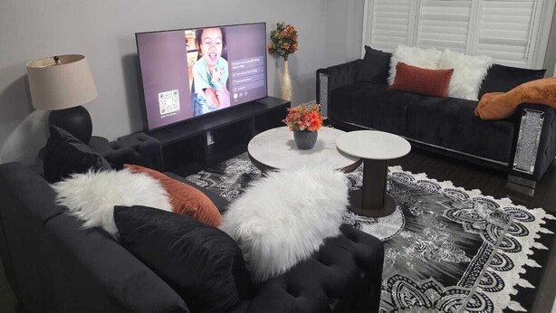 Een moderne woonkamer met een flatscreen televisie, twee banken, een salontafel en een kamerkleed met dessin.