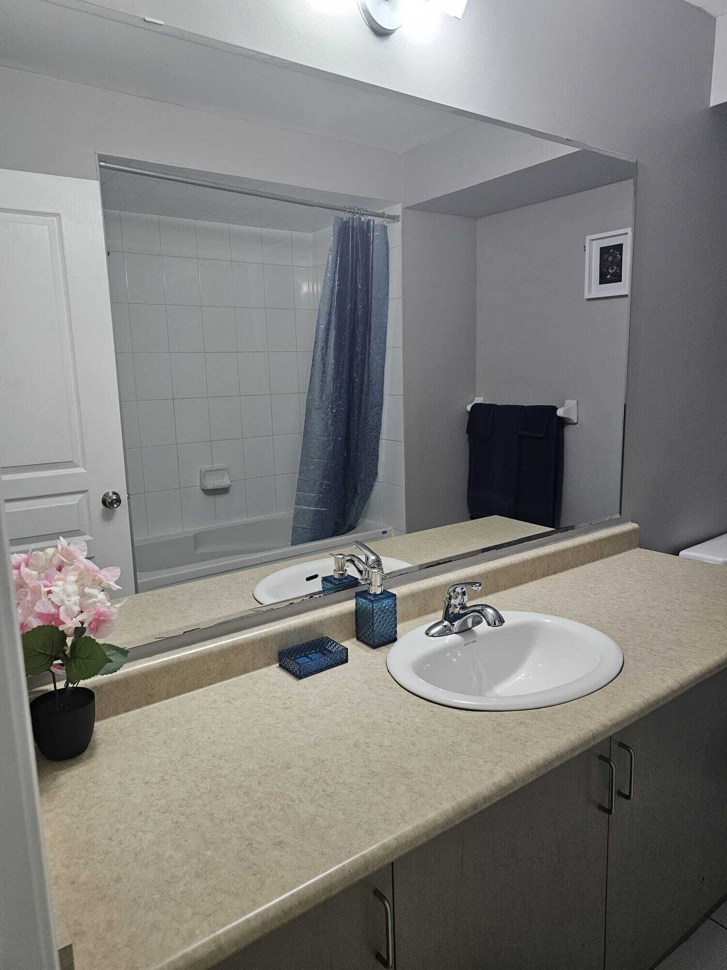 Une salle de bain avec un lavabo blanc, un miroir, une douche avec un rideau bleu et un petit porte-serviettes.