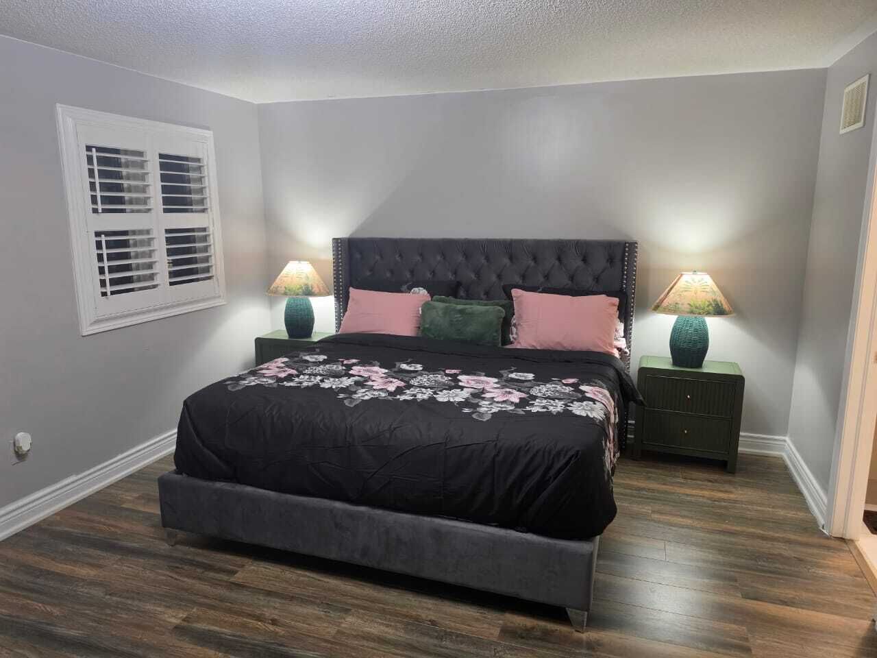 Une chambre à coucher avec un lit, deux tables de chevet, une fenêtre avec des volets et une lampe sur chaque table de chevet.