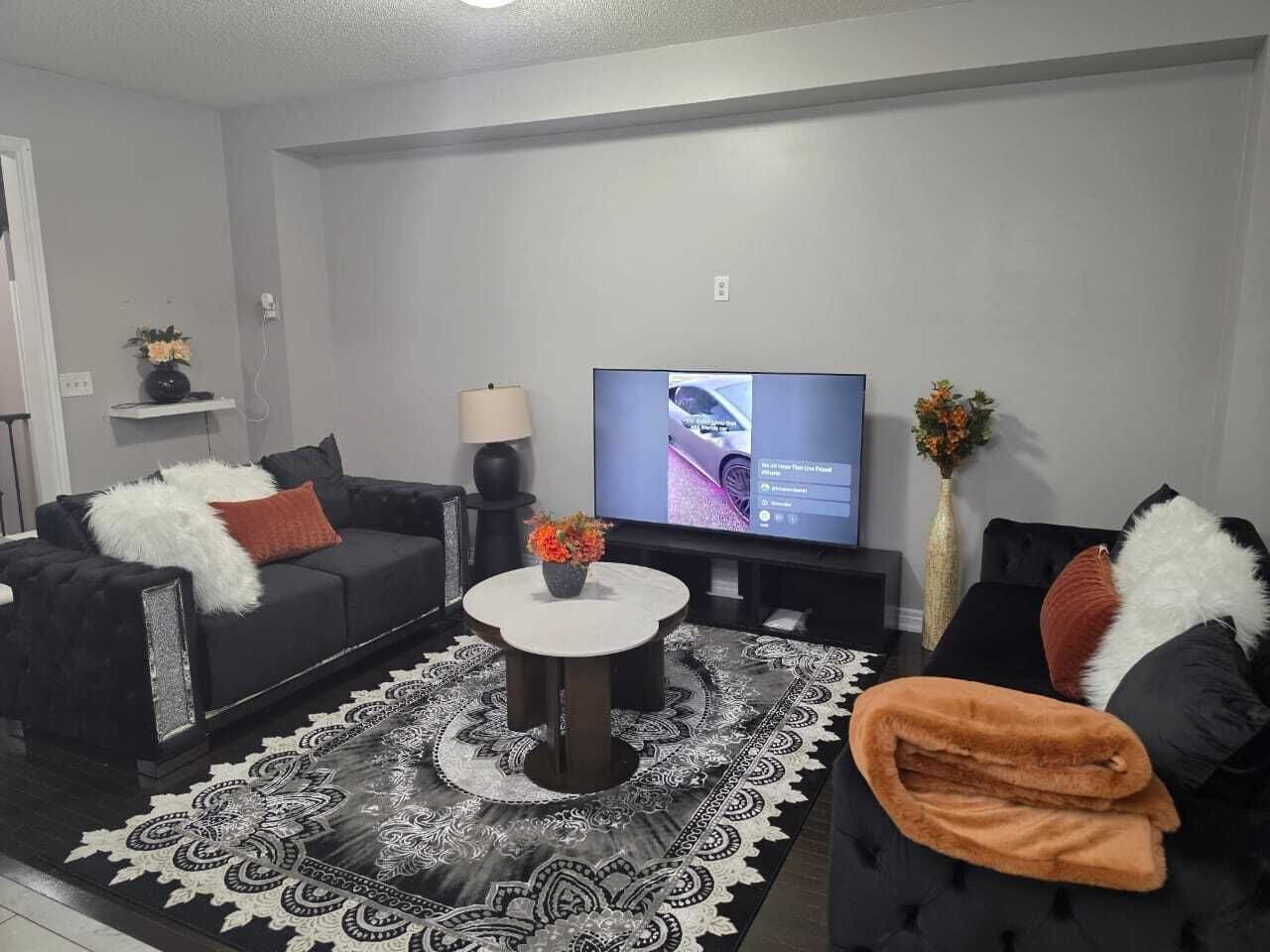 Uma sala de estar moderna com televisão de tela plana, um sofá, uma mesa de centro e um tapete estampado.