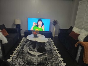 Una sala de estar con una televisión de pantalla plana, dos sofás, una mesa de centro y un tapete estampado.