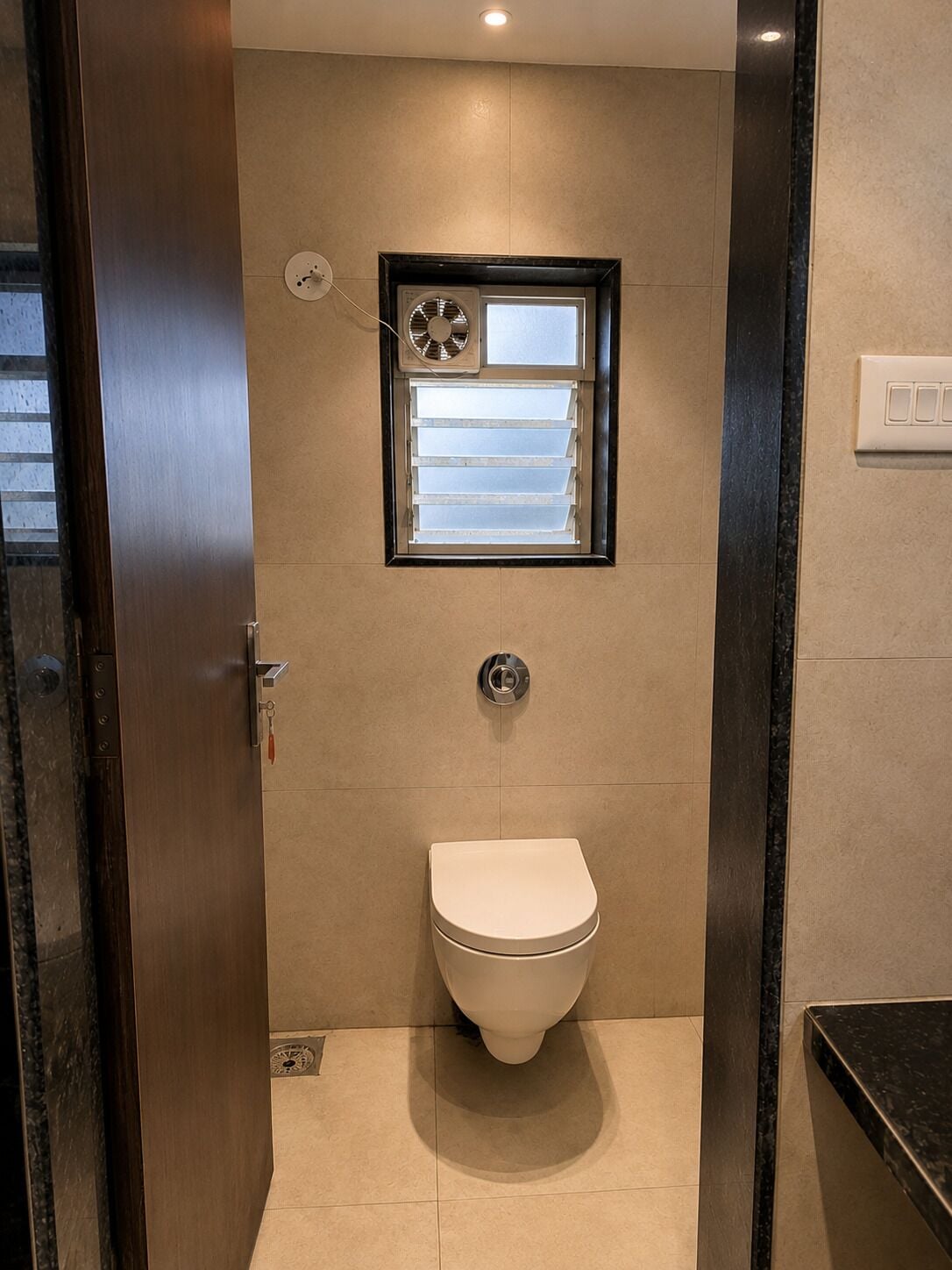 A bathroom with a toilet, a window with blinds, and a wall-mounted air conditioning unit.