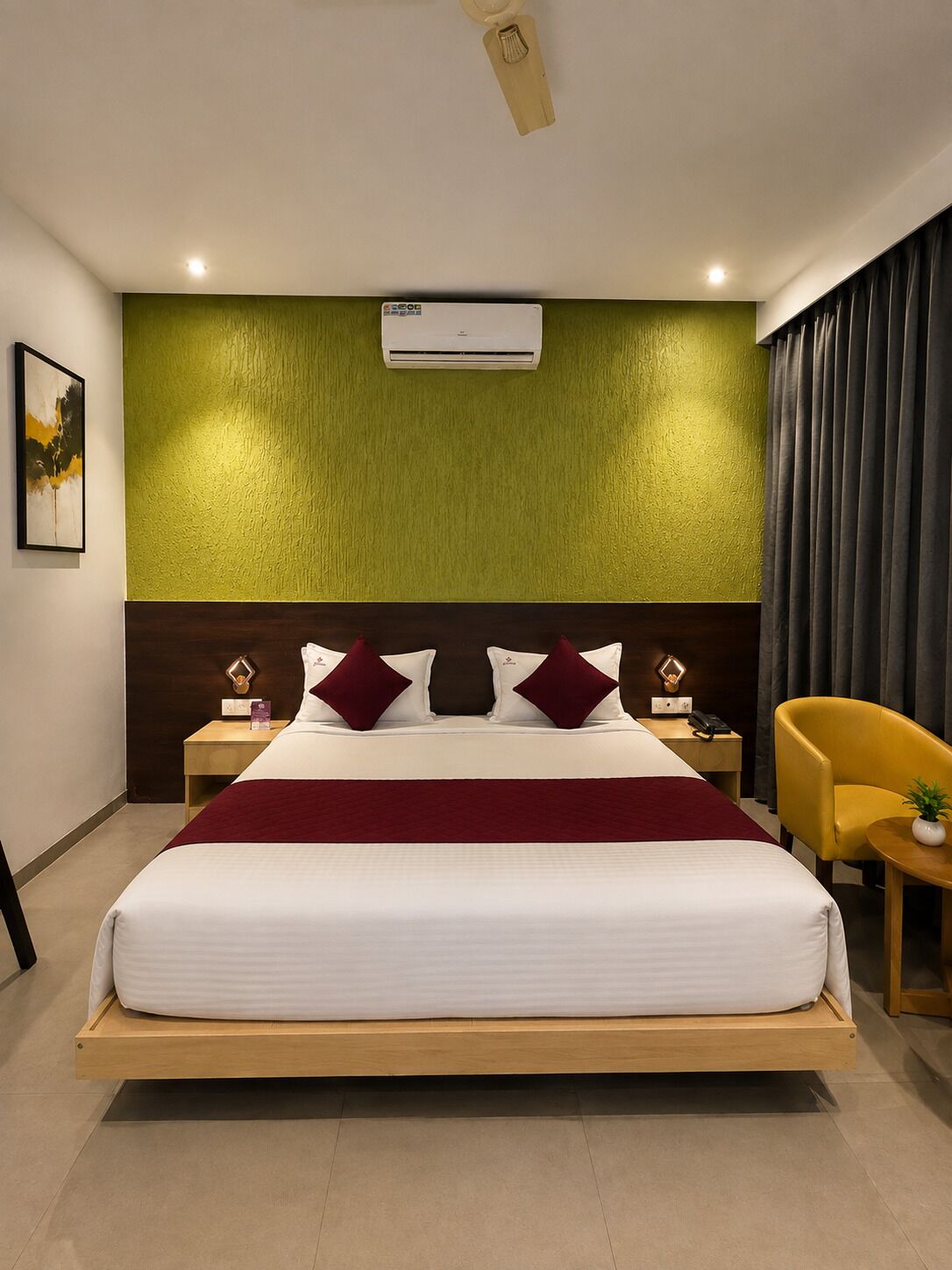 A modern hotel room with a bed, bedside tables, a chair, and an air conditioning unit.