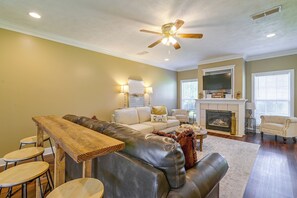 Ein Wohnzimmer mit Ecksofa, Couchtisch aus Holz, Kamin und einem darüber montierten Fernseher.