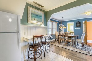 A dining area with a table and chairs, a refrigerator, and a painting on the wall.