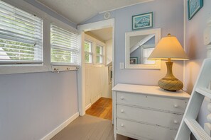 A narrow hallway with a white dresser, a lamp, and a mirror on the wall.