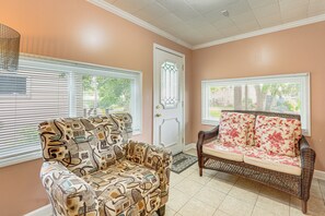 A room with a patterned armchair, a sofa with floral cushions, and a door with a decorative glass panel.