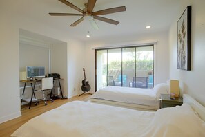 Ein Schlafzimmer mit zwei Betten, einem Schreibtisch mit Computer, einer Gitarre und einem Balkon mit Stühlen.